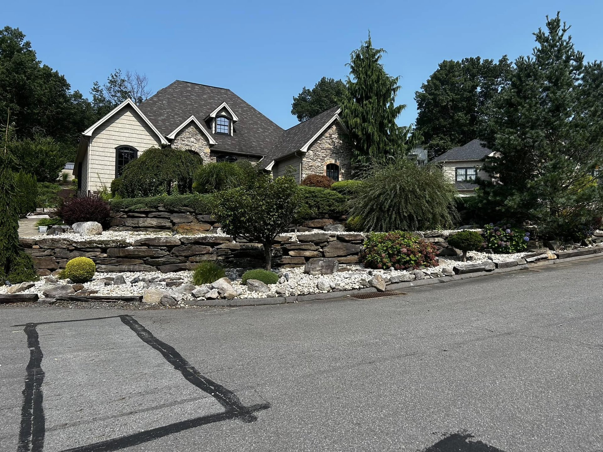 Stone house with landscaped front yard and driveway under a clear sky