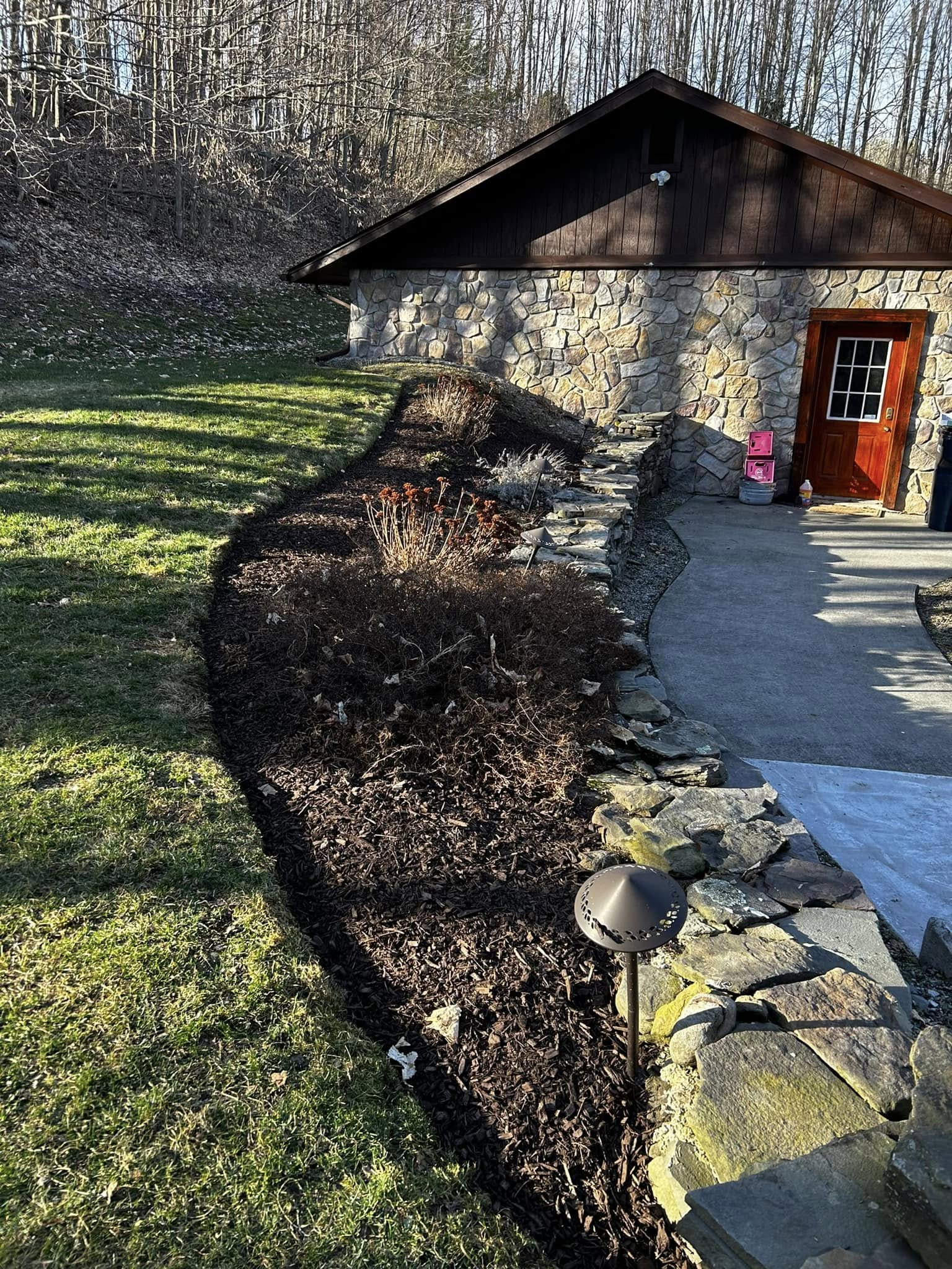 Stone house with red door, gravel path, and curved hedge in a sunny yard