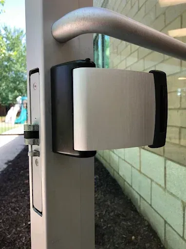 Close-up of a silver and black door-mounted security locking device on a commercial glass door.