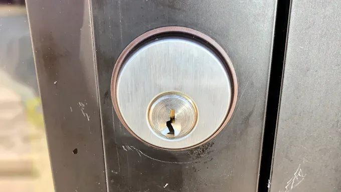 A close-up of a silver-colored deadbolt lock set into a dark metal door frame.