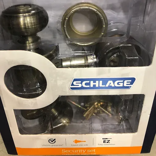 A Schlage security door handle and lock set in a retail package with bronze-toned hardware and installation components.