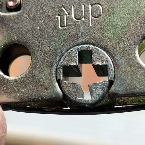 Close-up of a gold-toned metal mechanism showing a centered cross-shaped screw head and the embossed word 