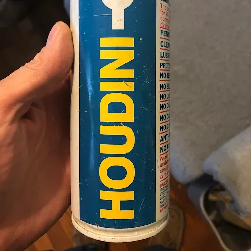 A hand holds a tall aerosol can labeled 