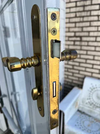A side view of a brass door handle assembly with a latch mechanism mounted on the edge of a white door.