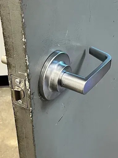 A close-up view of a brushed metal lever-style door handle on a gray commercial door.