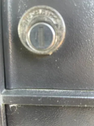A close-up of a circular, metallic keyhole set into a dark, textured metal surface.