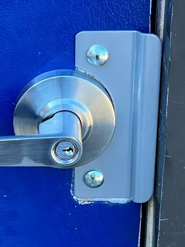 A metal lever-style door handle with a keyhole mounted on a blue door with a gray protective security plate.