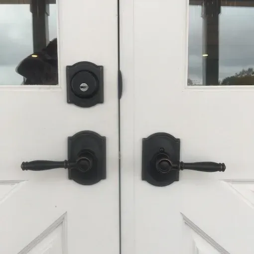 Double white doors with matte black levers and a deadbolt, with a blurred silhouette visible through the window pane.