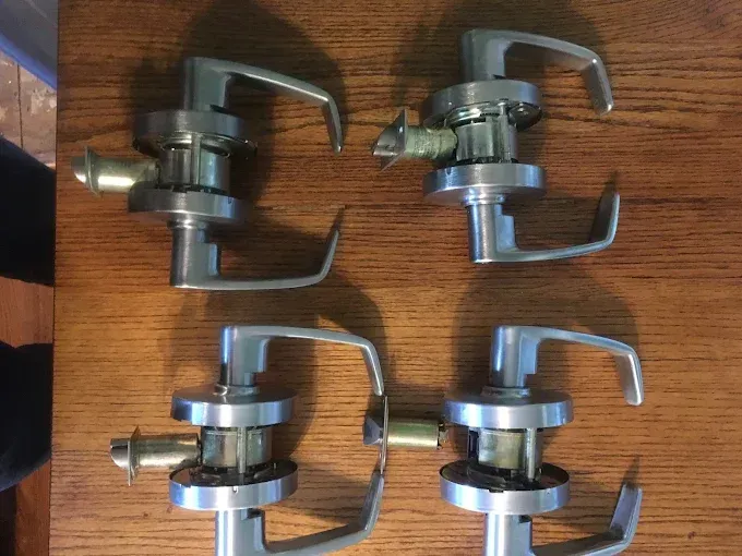 Four silver commercial lever-style door handles arranged on a wooden surface.