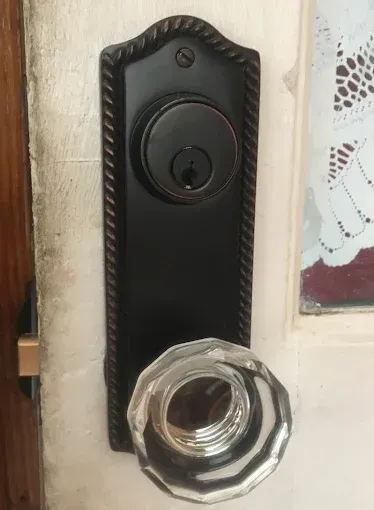 A matte black door handle set with a rope-textured border and a clear, multifaceted glass knob on a white door.