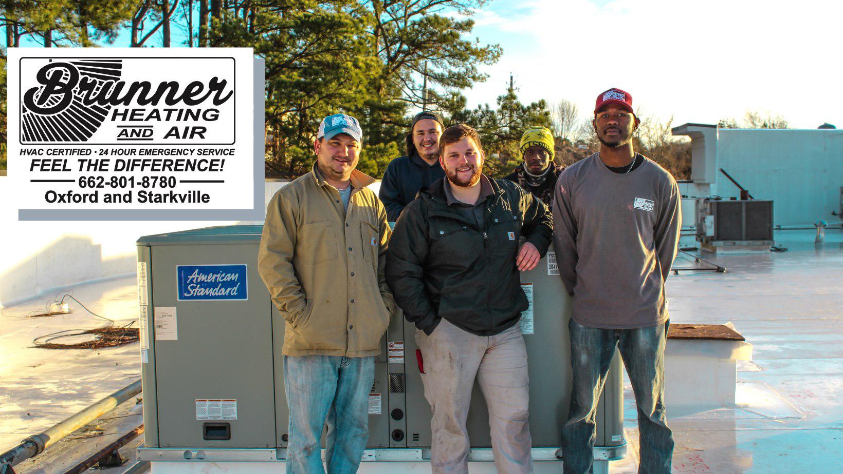 Four employees from Brunner Heating and Air pose on a rooftop next to a large HVAC unit on a sunny day.