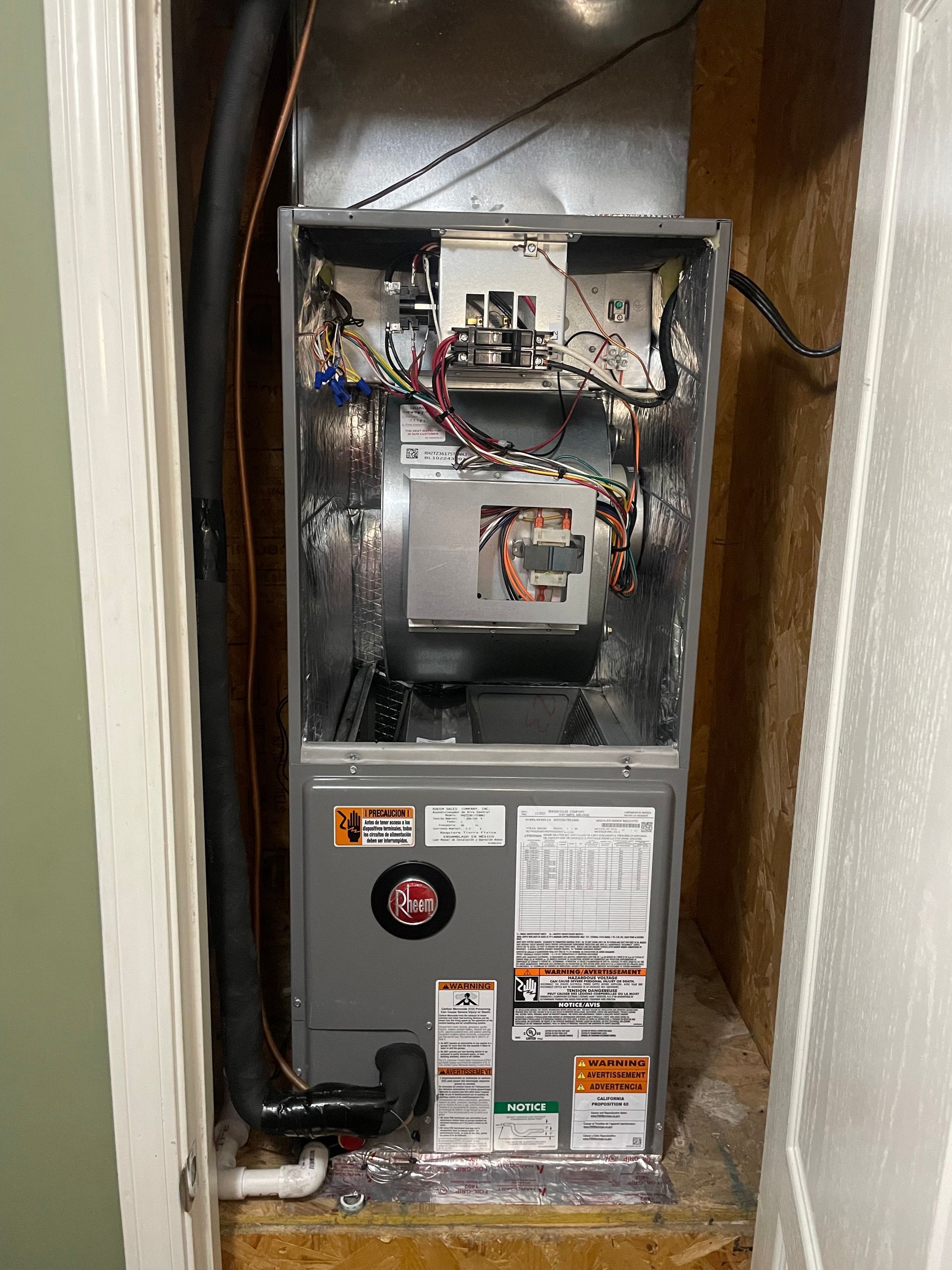 An indoor HVAC unit with its front panels removed, revealing the blower motor, wiring, and metal interior components.