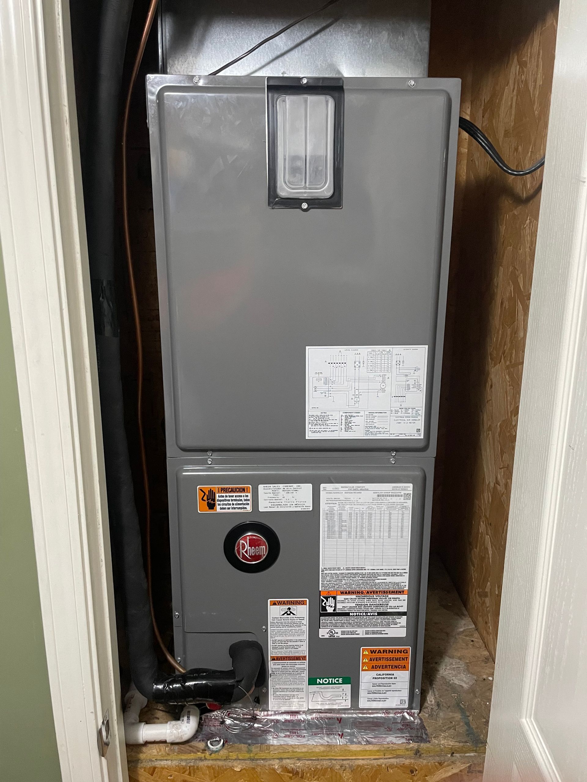 A grey HVAC air handler unit installed in a small, narrow closet space.