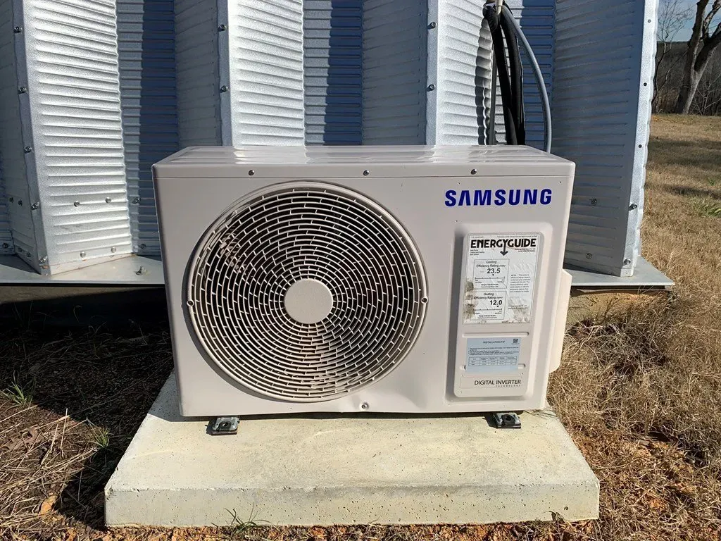 A white Samsung outdoor air conditioner unit sitting on a concrete pad outdoors.