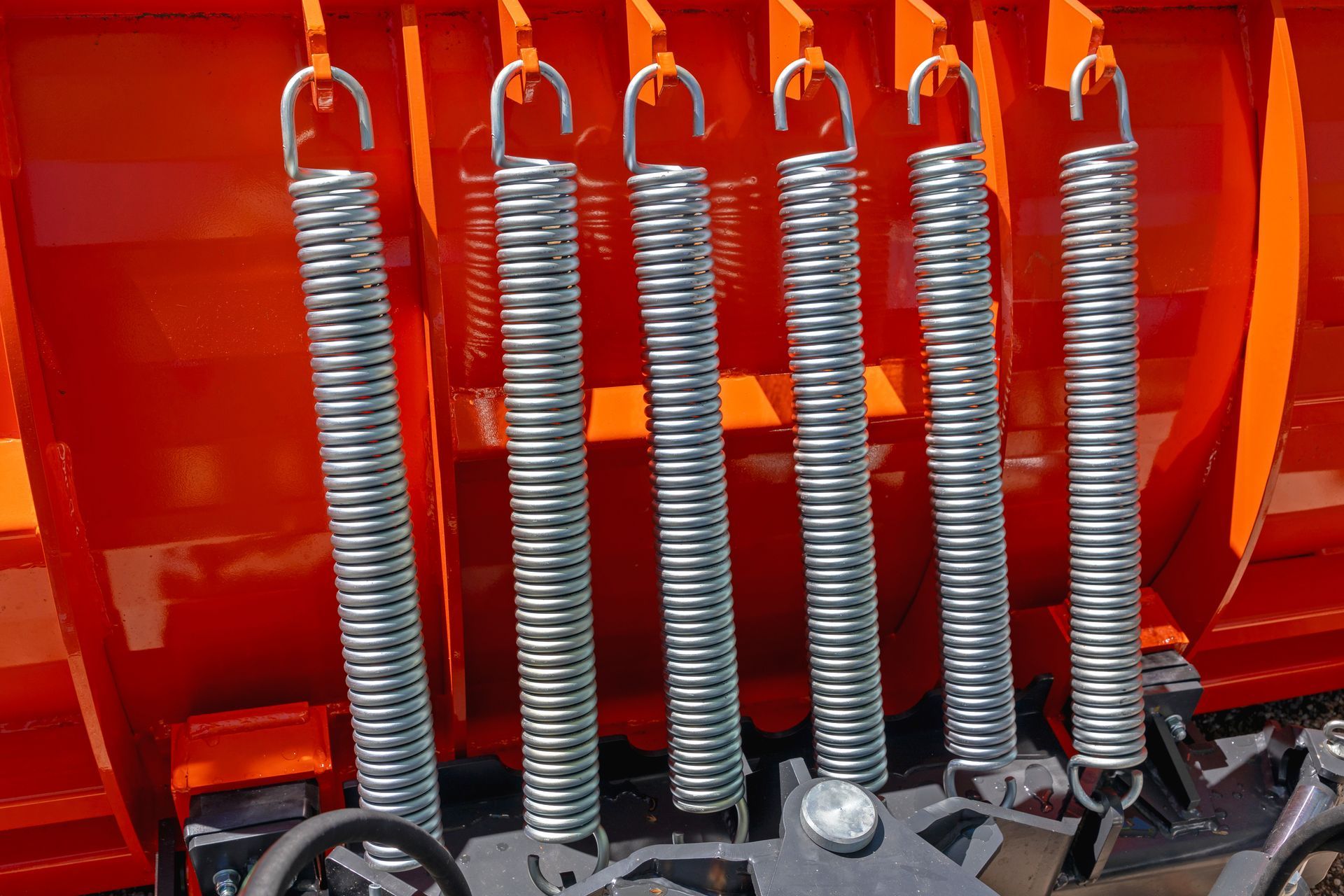Row of heavy-duty extension springs with hooks mounted on orange equipment.