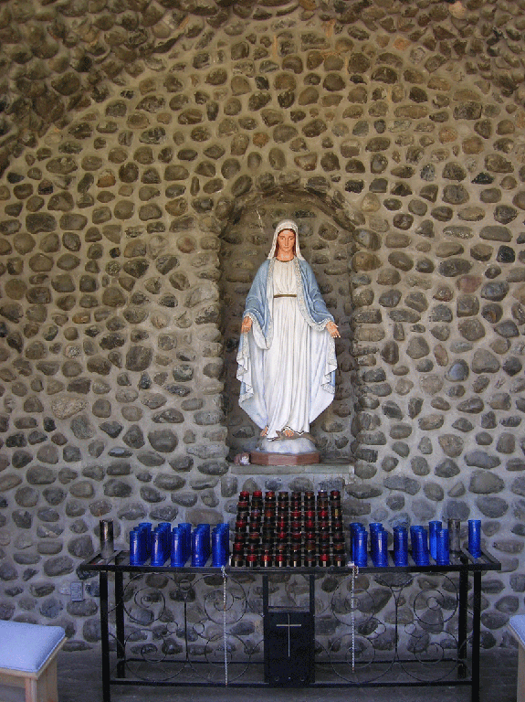 Statue of Virgin Mary in a stone alcove, surrounded by votive candles; light blue and white robes.