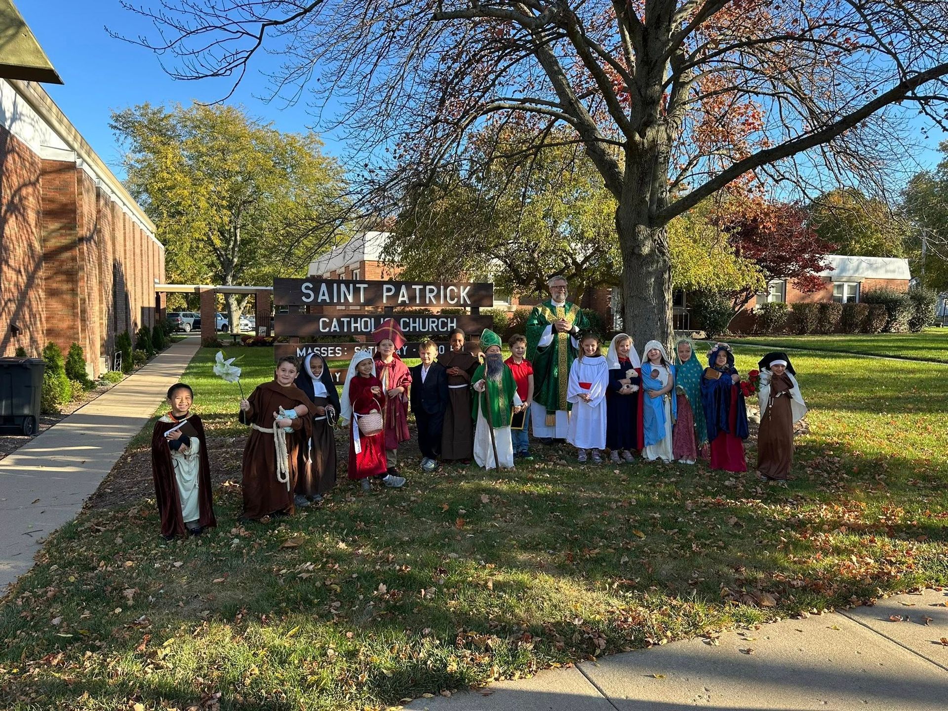 Children in costumes pose on a lawn in front of St. Patrick Church. Brown sign is visible.