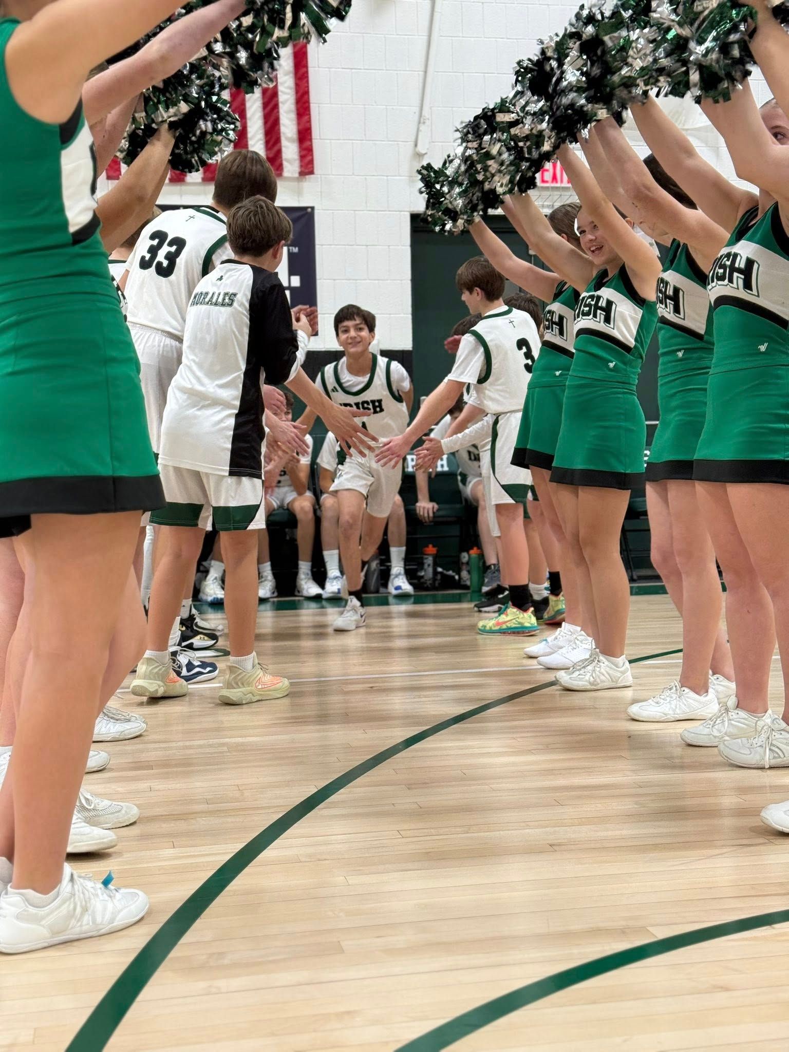 Youth cross country team posing on a wooden floor, wearing green uniforms with white lettering.
