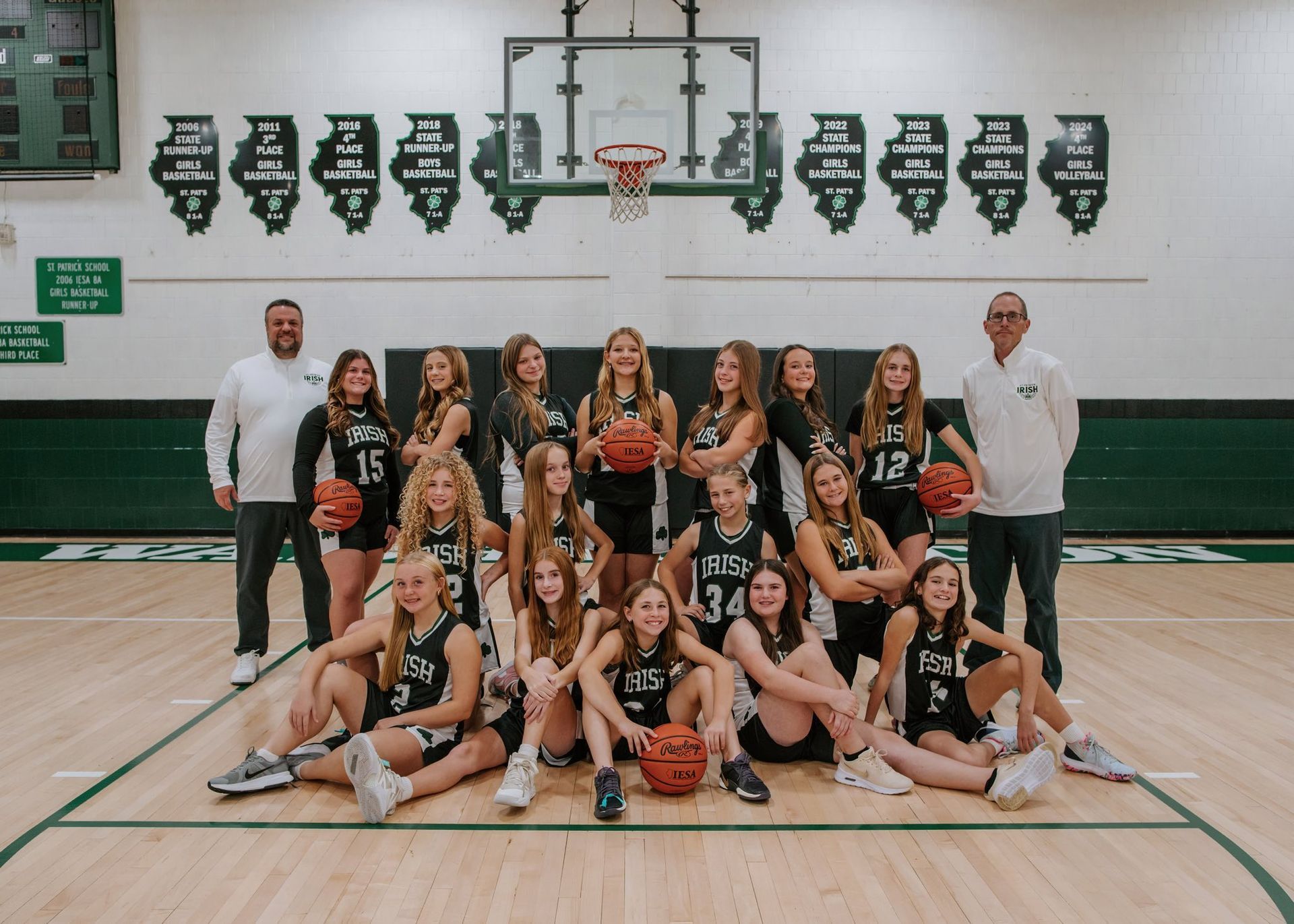 High school girls' basketball team posed with coaches on court; wearing green and black uniforms.