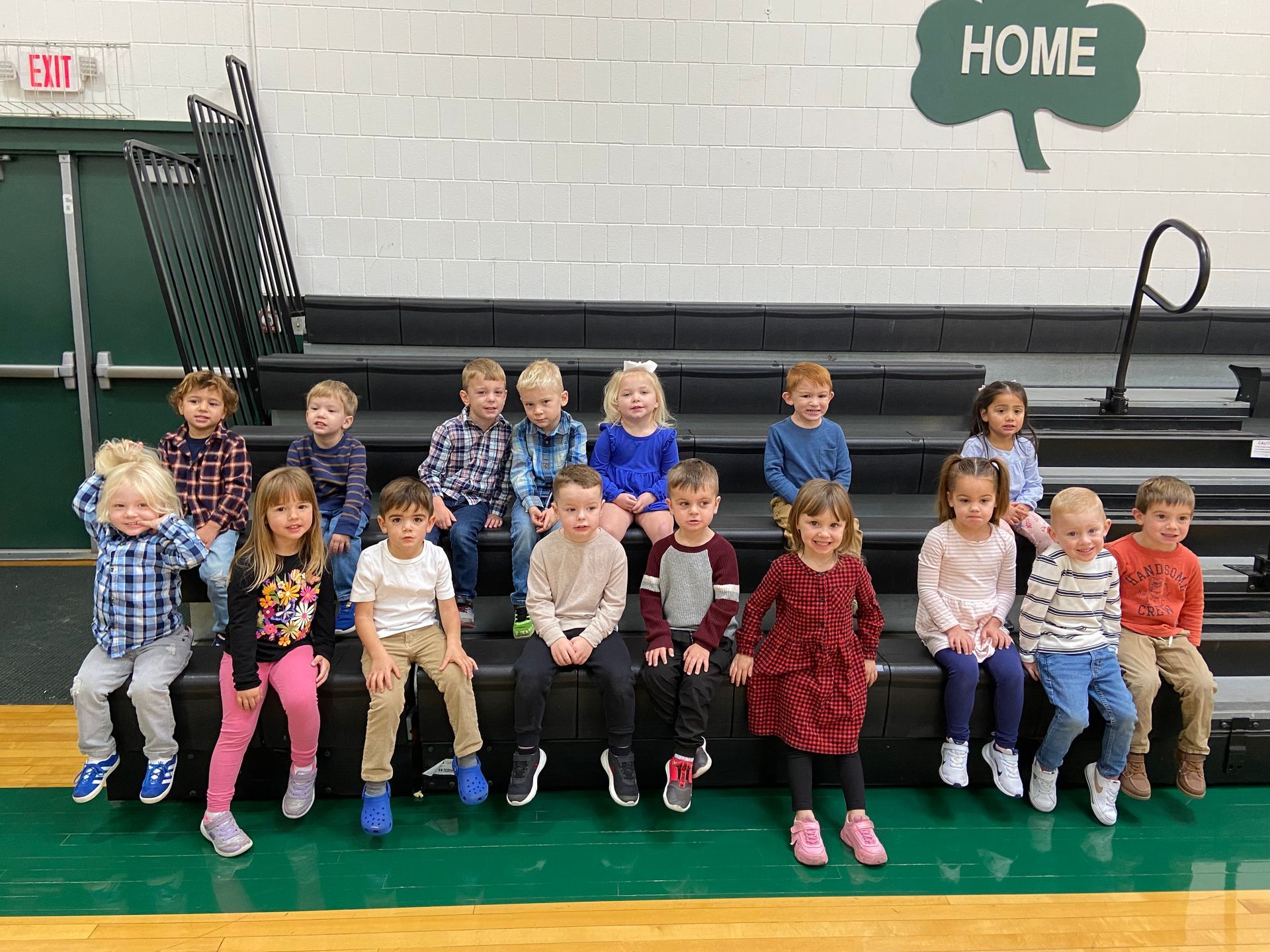 Children sitting on bleachers in a gymnasium. Some smiling at the camera.
