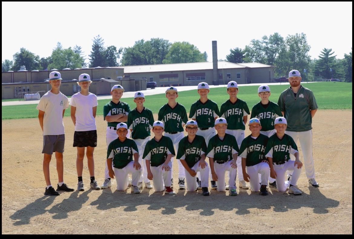 Youth baseball team wearing green jerseys, kneeling and standing on a baseball field.