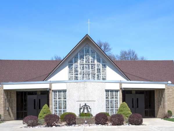 Church exterior with stained glass, a cross, and bell, on a sunny day.