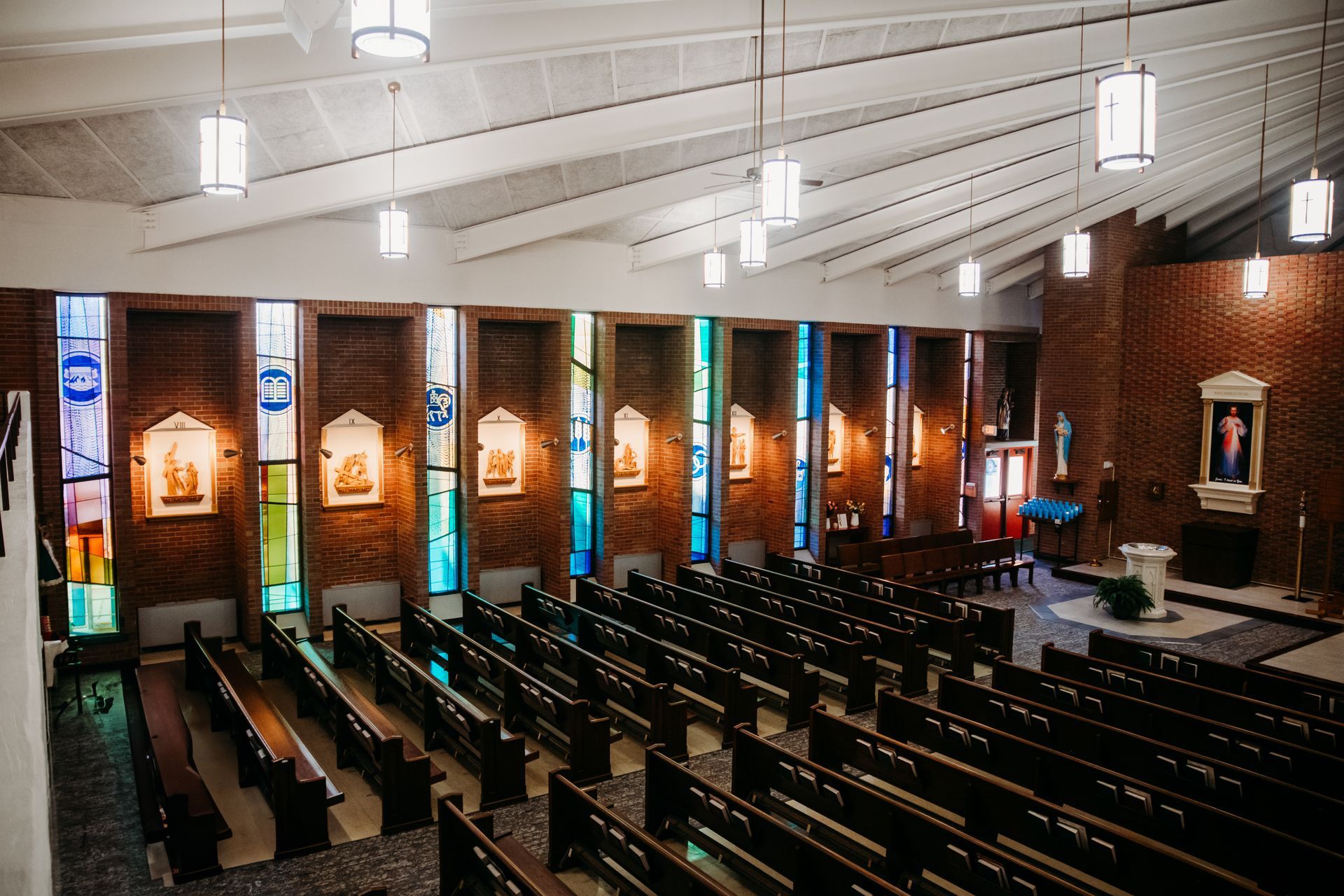 Interior view of a church with pews, stained glass windows, and a brick wall.