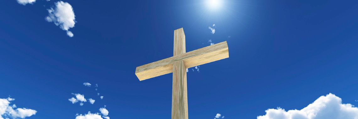 Wooden cross against a bright blue sky with white clouds and the sun.