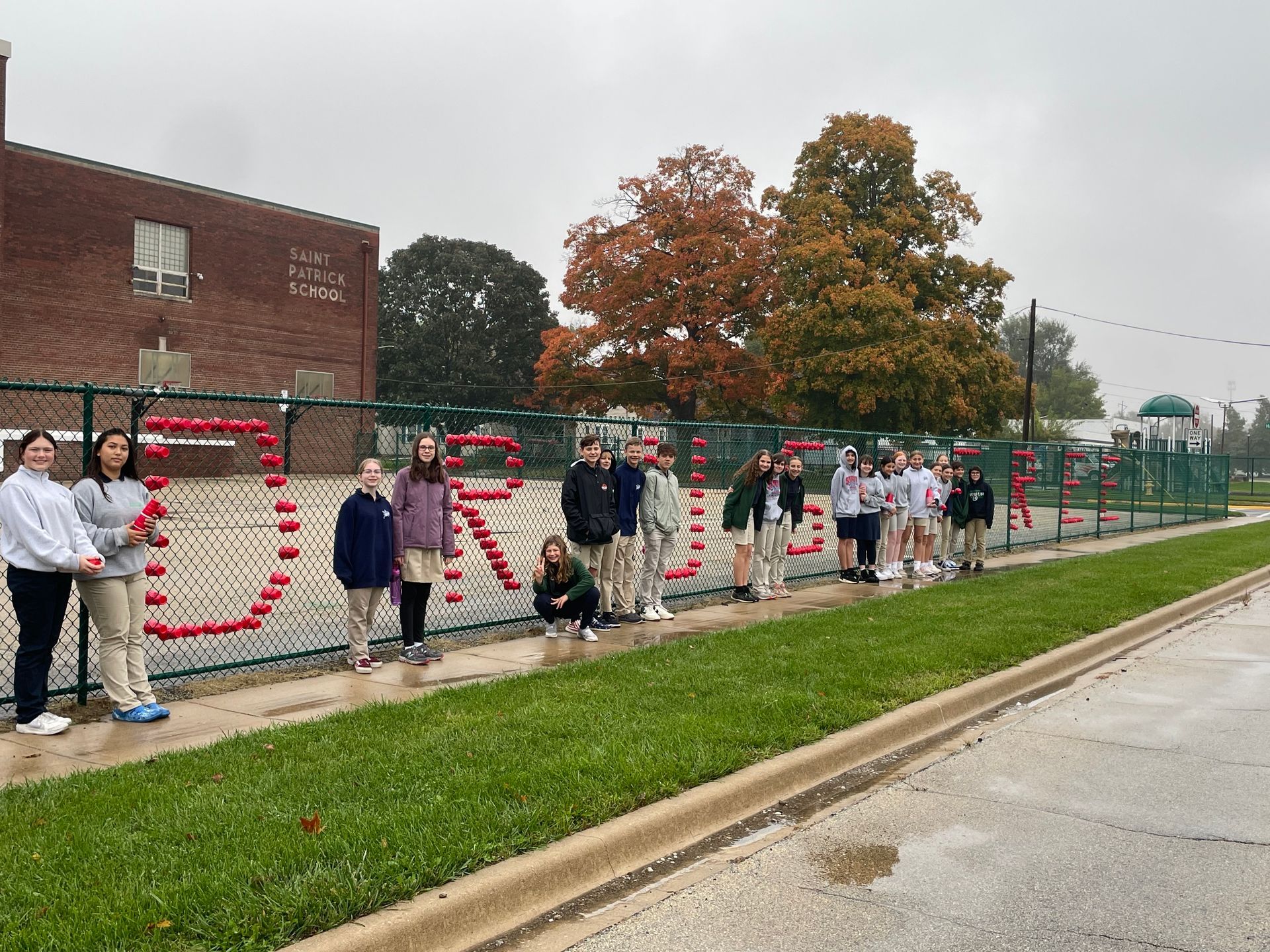 Students pose beside a fence spelling
