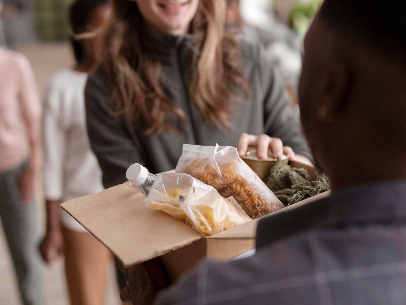 Man hands box of food to woman, smiling, in a donation event.