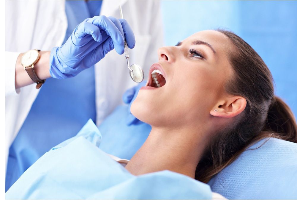 Woman in dentist's chair, mouth open, being examined by a dentist wearing gloves.