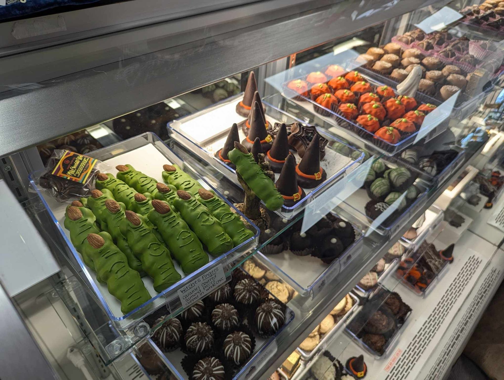 A display case filled with Halloween chocolates, including green witch fingers, orange balls, and chocolate cones.