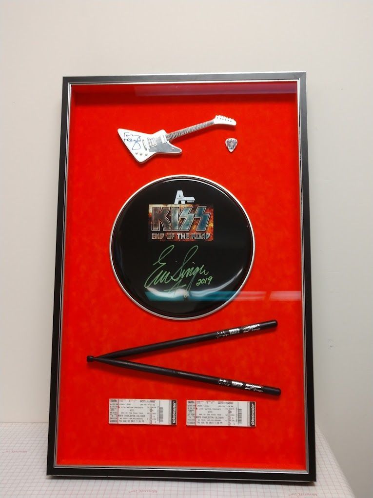 Framed Elvis Presley memorabilia: silver guitar, drum, signature, chopsticks, and tickets, set against red velvet.