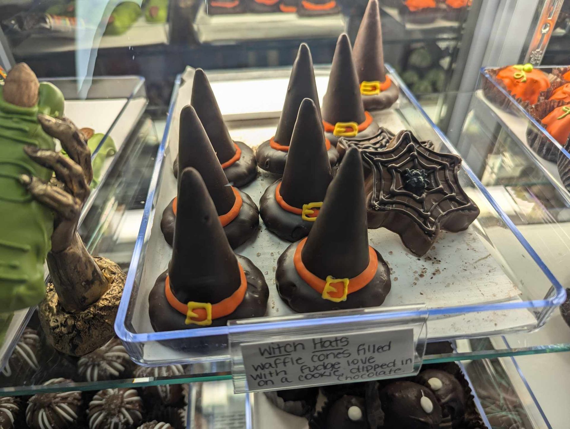 Witch hat-shaped chocolate treats with orange buckles on display in a glass case.