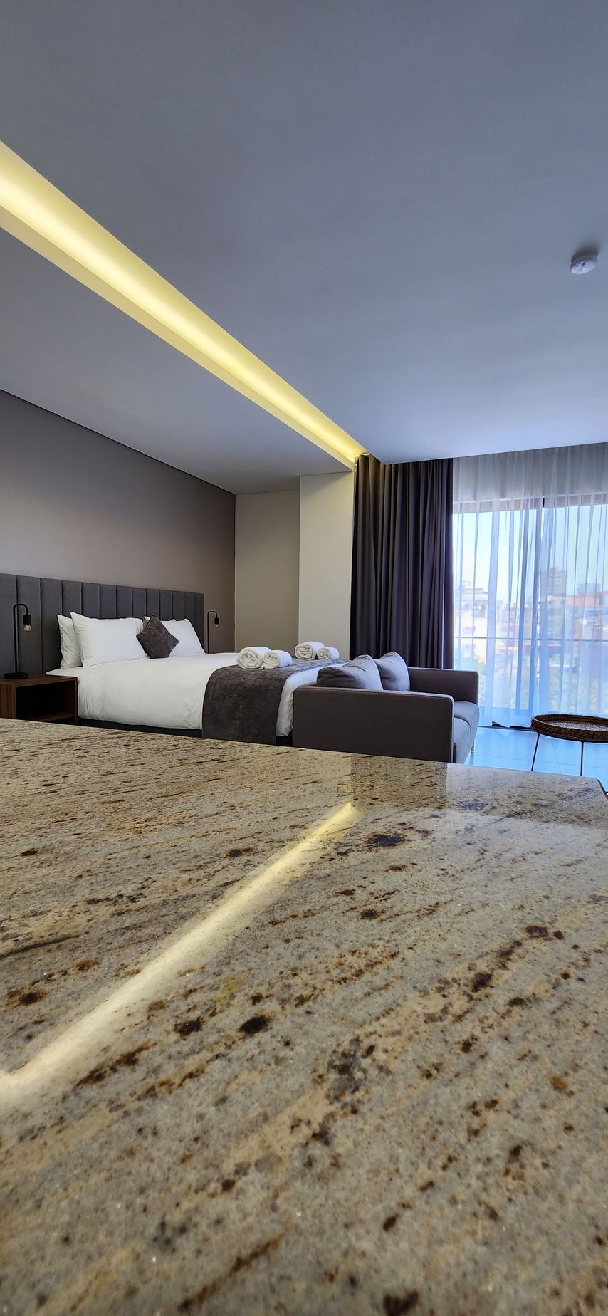 Bedroom with a large bed, dark curtains, and a granite-like surface in the foreground.