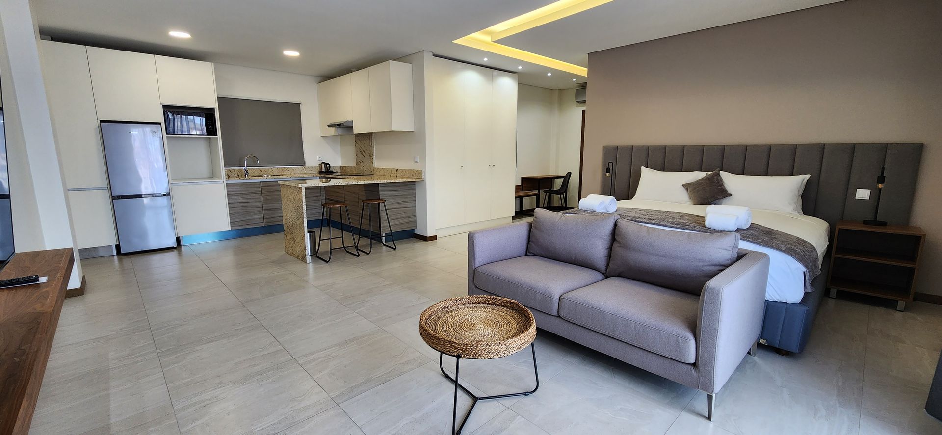A modern studio apartment with a kitchen, sofa, bed, and small coffee table.
