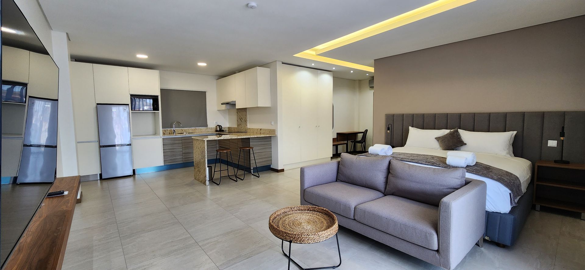 Open concept apartment with kitchen, living area, and bed; neutral tones.