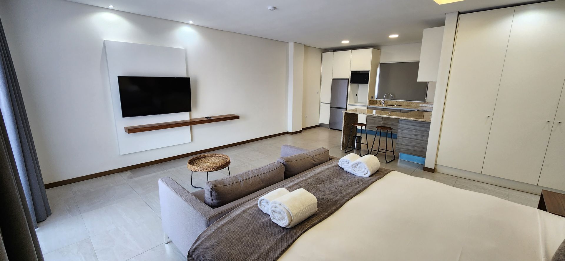 Modern studio apartment with minimalist decor, featuring a bed, sofa, kitchen, and TV.