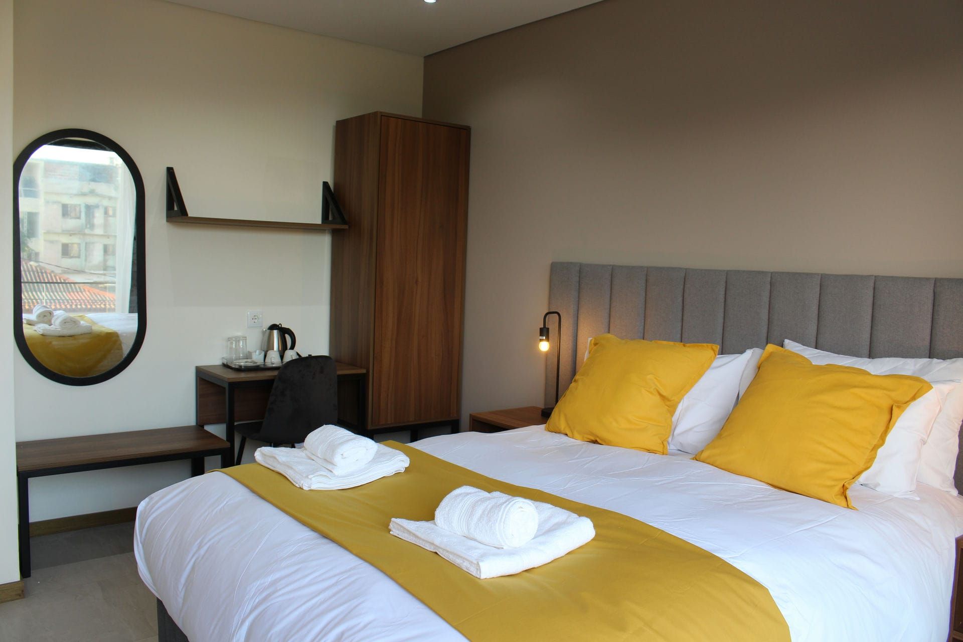 Bedroom with bed, yellow accents, mirror, desk, wooden wardrobe.