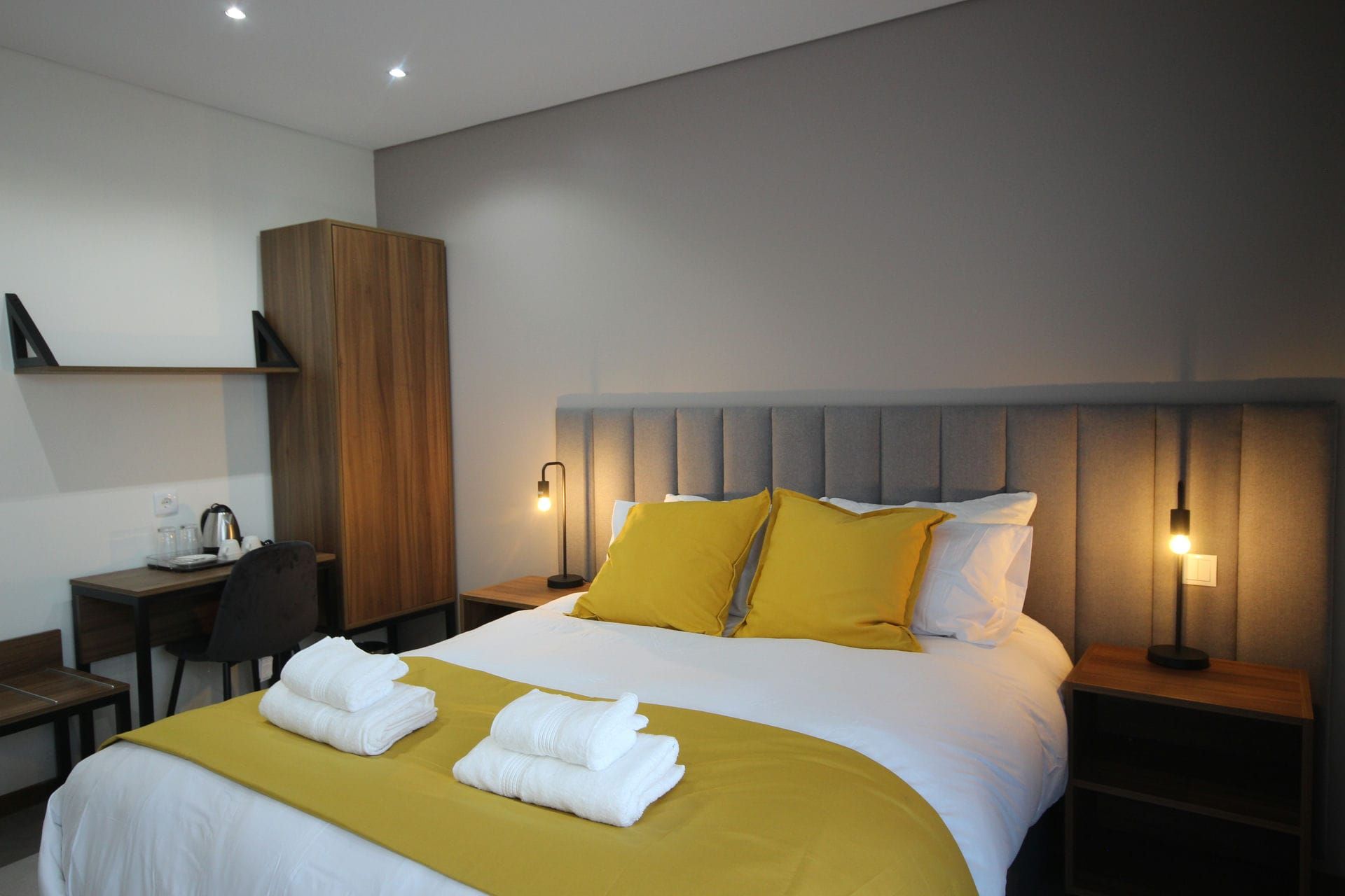 Bedroom with bed, yellow accents, nightstands, wooden wardrobe, and desk.