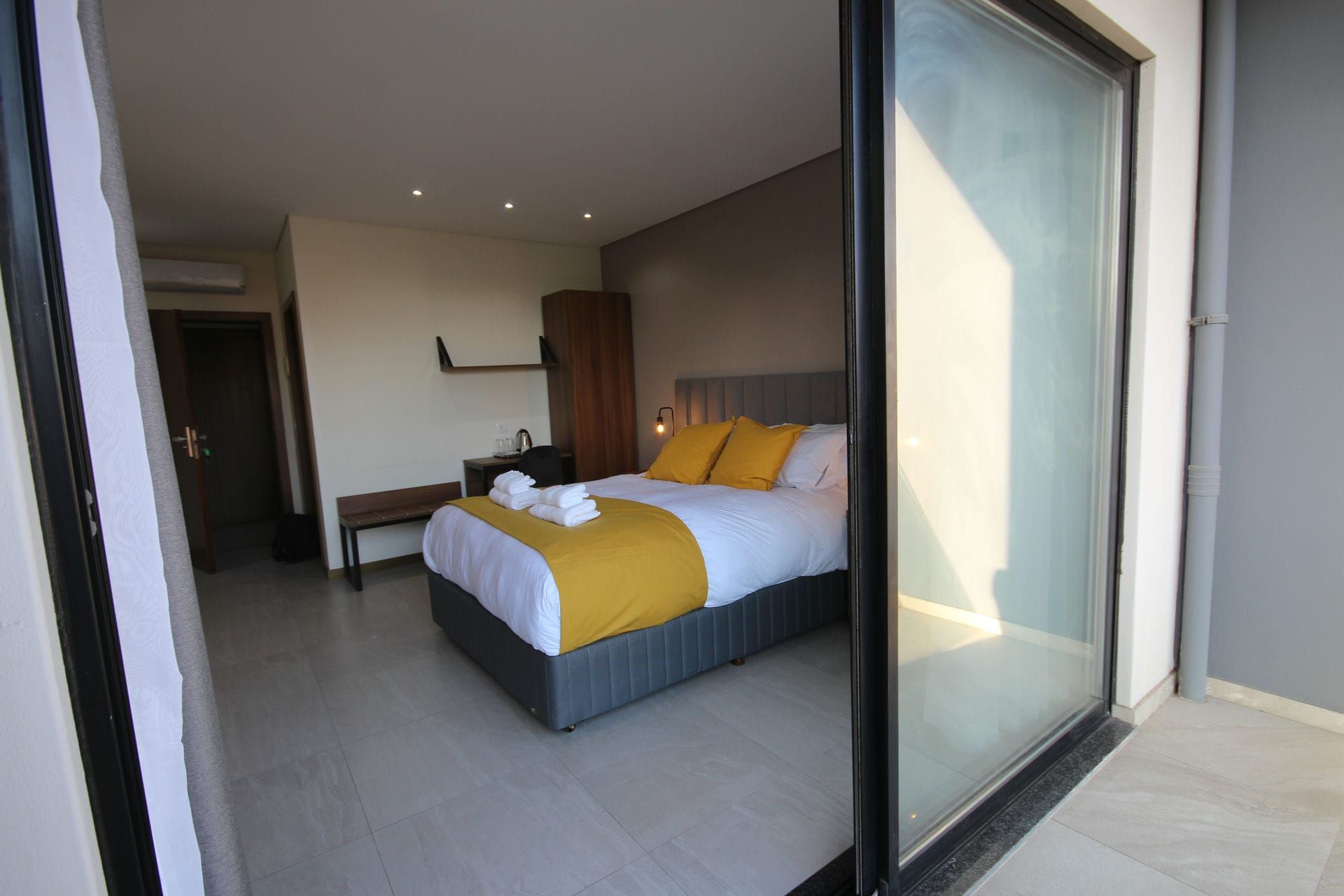 Bedroom interior, bed with yellow accents, visible through sliding glass door.