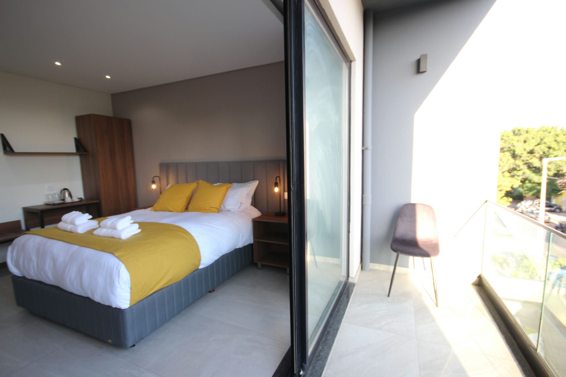 Bedroom with a bed, yellow accents, and open balcony door.