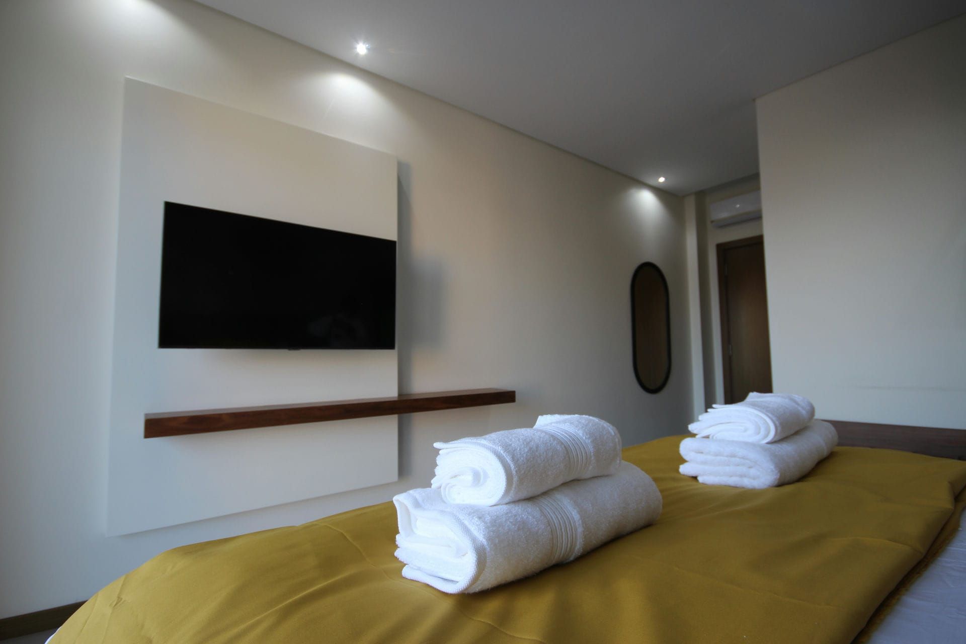 Bedroom with TV, white towels on bed with yellow cover, and mirror.