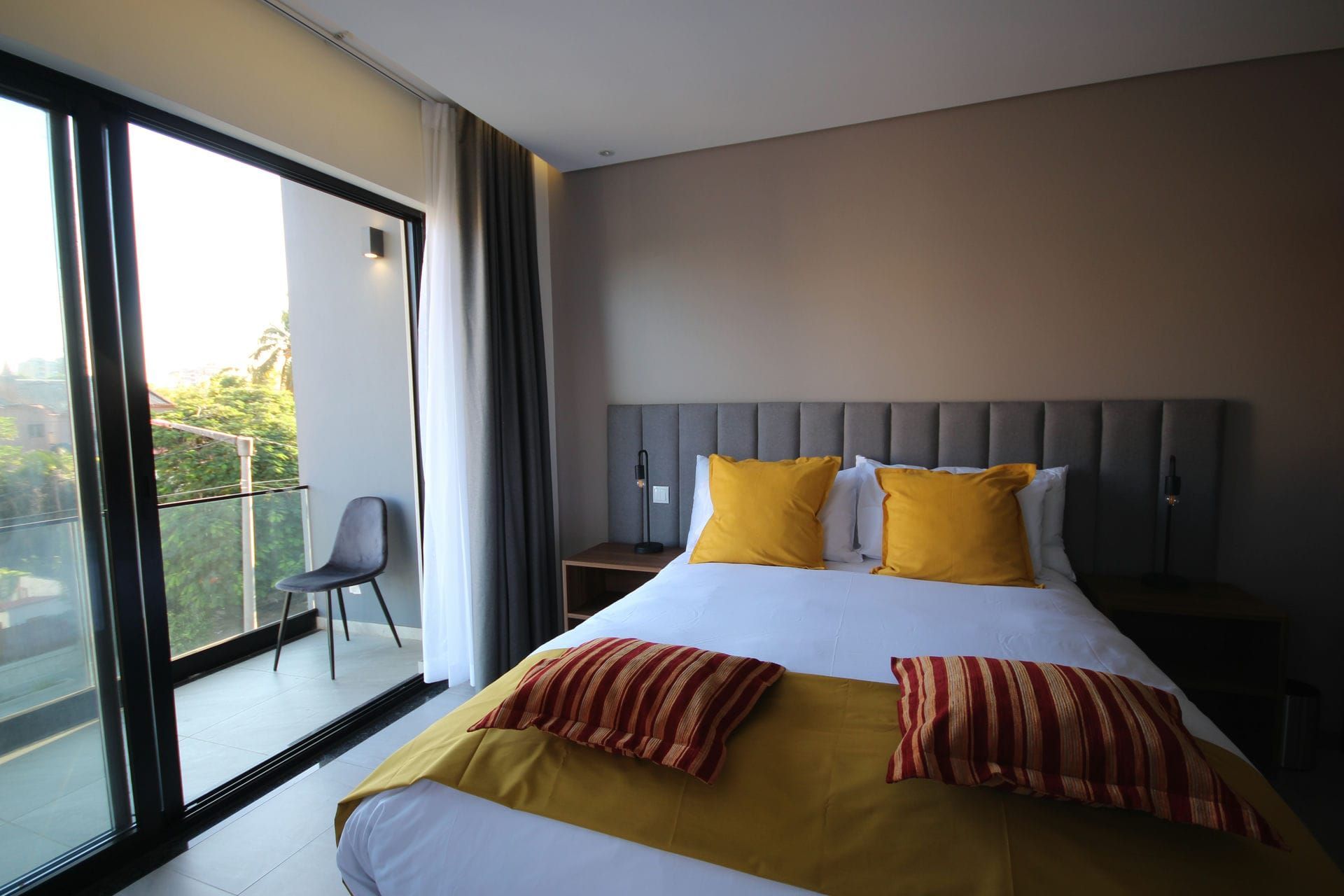 Bedroom with bed, yellow pillows, sliding glass door to balcony with chair.