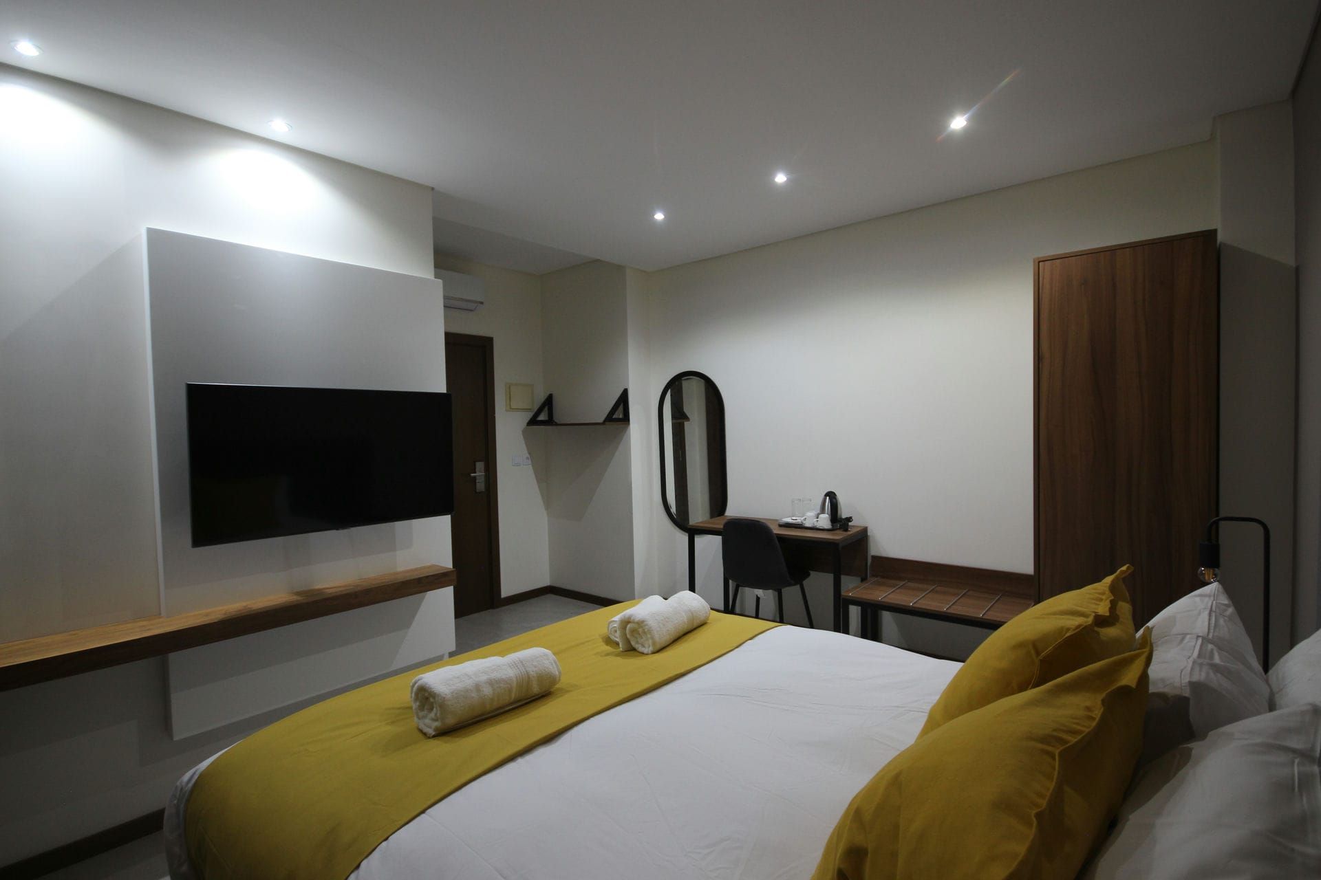 Bedroom interior with a bed, TV, desk, and wardrobe. Neutral walls, yellow accents.