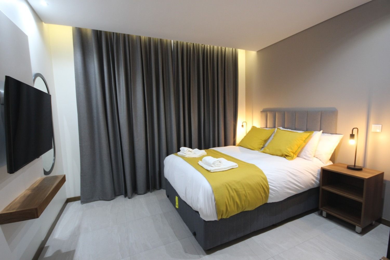 Bedroom with a bed, yellow accents, curtains, television, and bedside table.