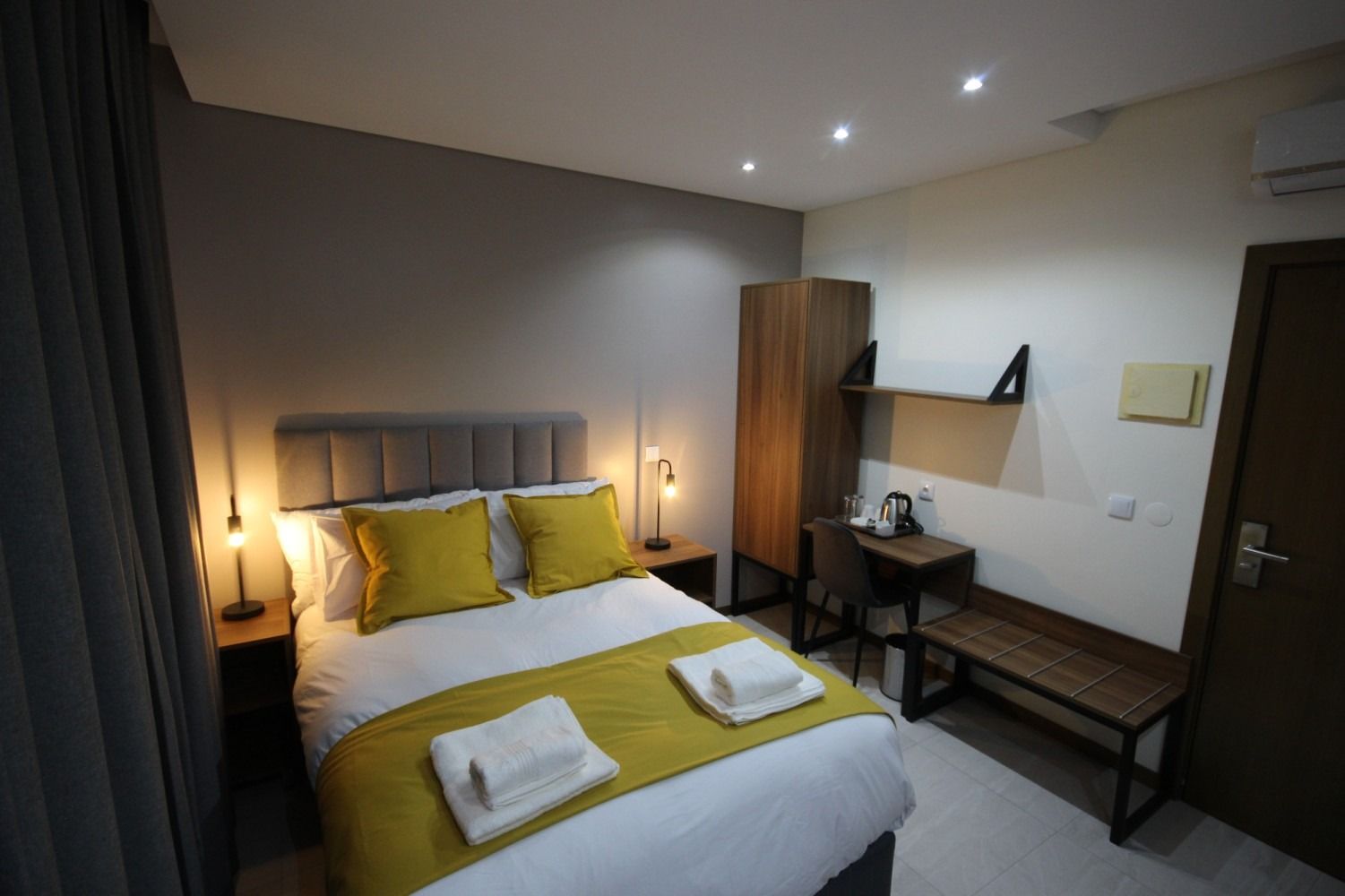 Bedroom with a bed, nightstands, wardrobe, small desk, bench, and window. Yellow and gray color scheme.
