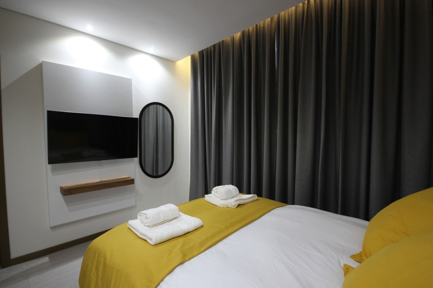Bedroom with a bed, TV, mirror, and gray curtains; yellow and white bedding and towels.