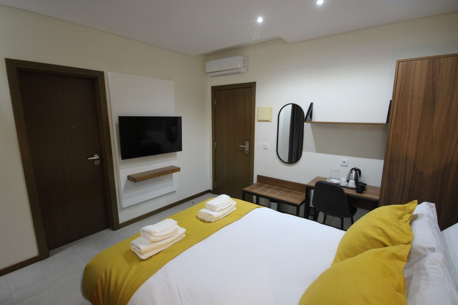 Hotel room with bed, desk, TV, and wardrobe. Yellow and white bedding. Brown doors and furniture.