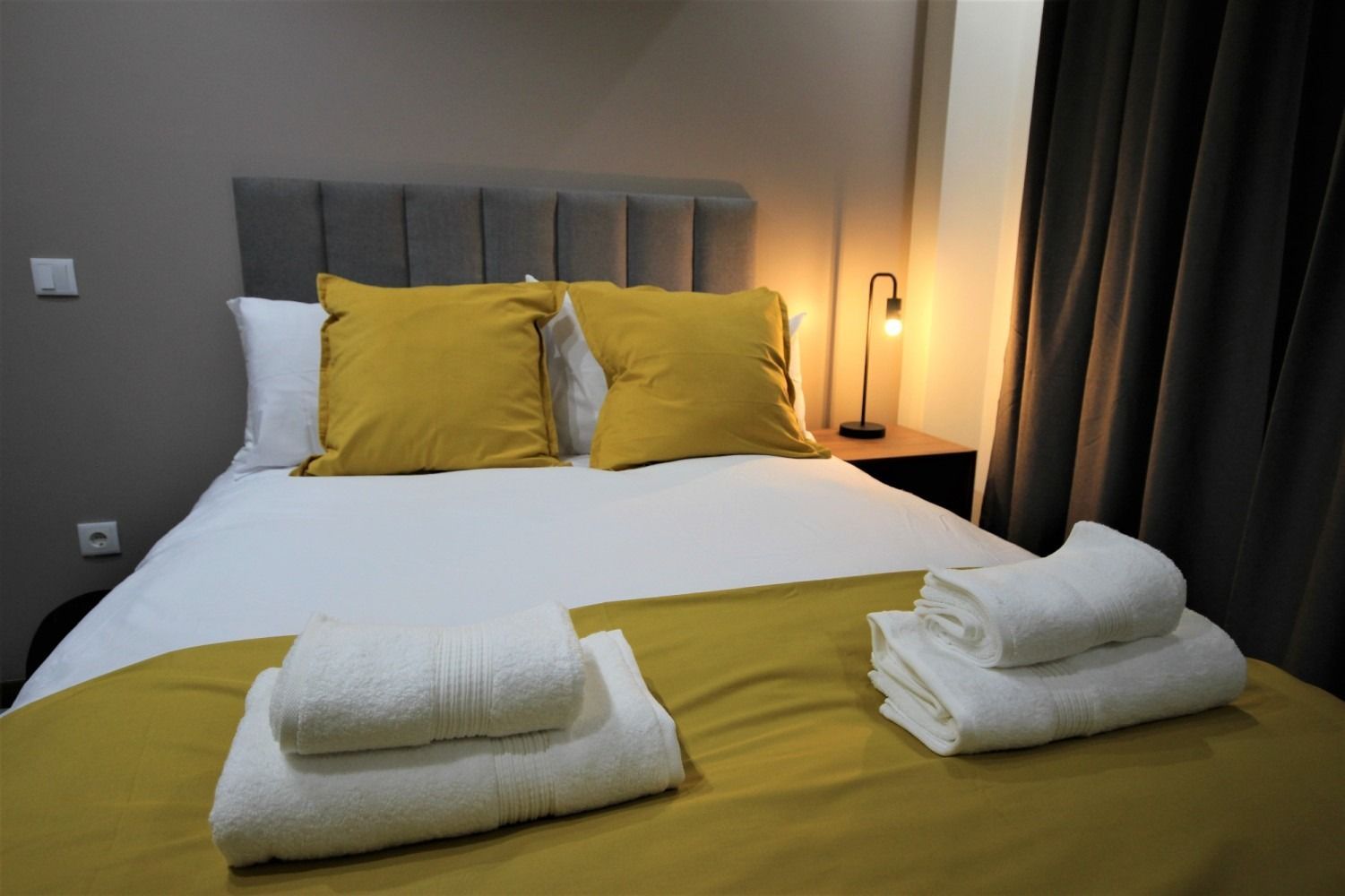 Bedroom with bed, yellow pillows, white towels, and a bedside lamp.